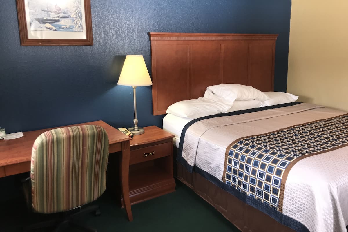 A hotel room with a bed, a desk with a chair, a lamp, and a framed picture on the wall.