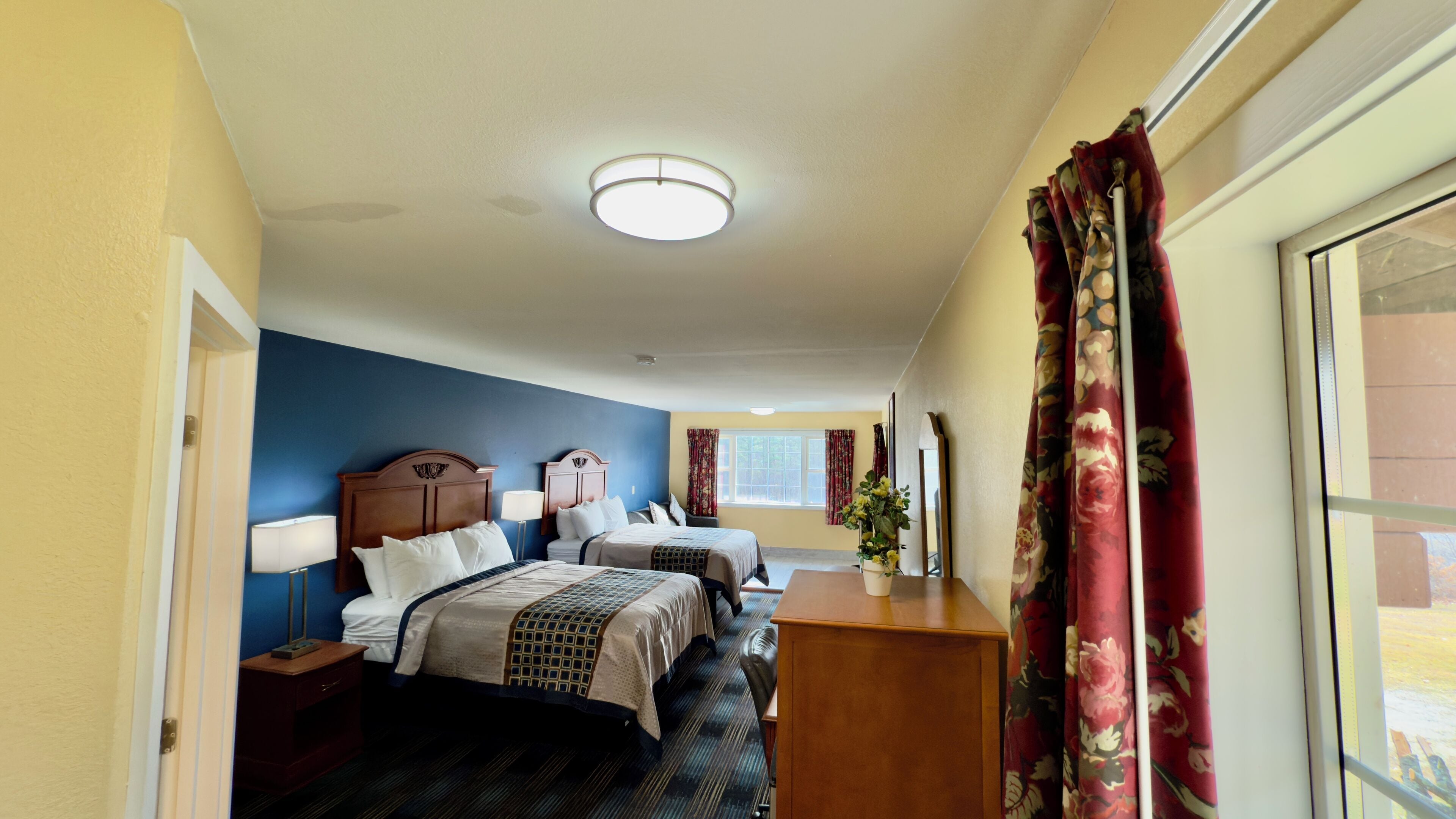 Ein Hotelzimmer mit zwei Betten, einem Schreibtisch, einem Fenster mit Vorhängen und einer Deckenleuchte.