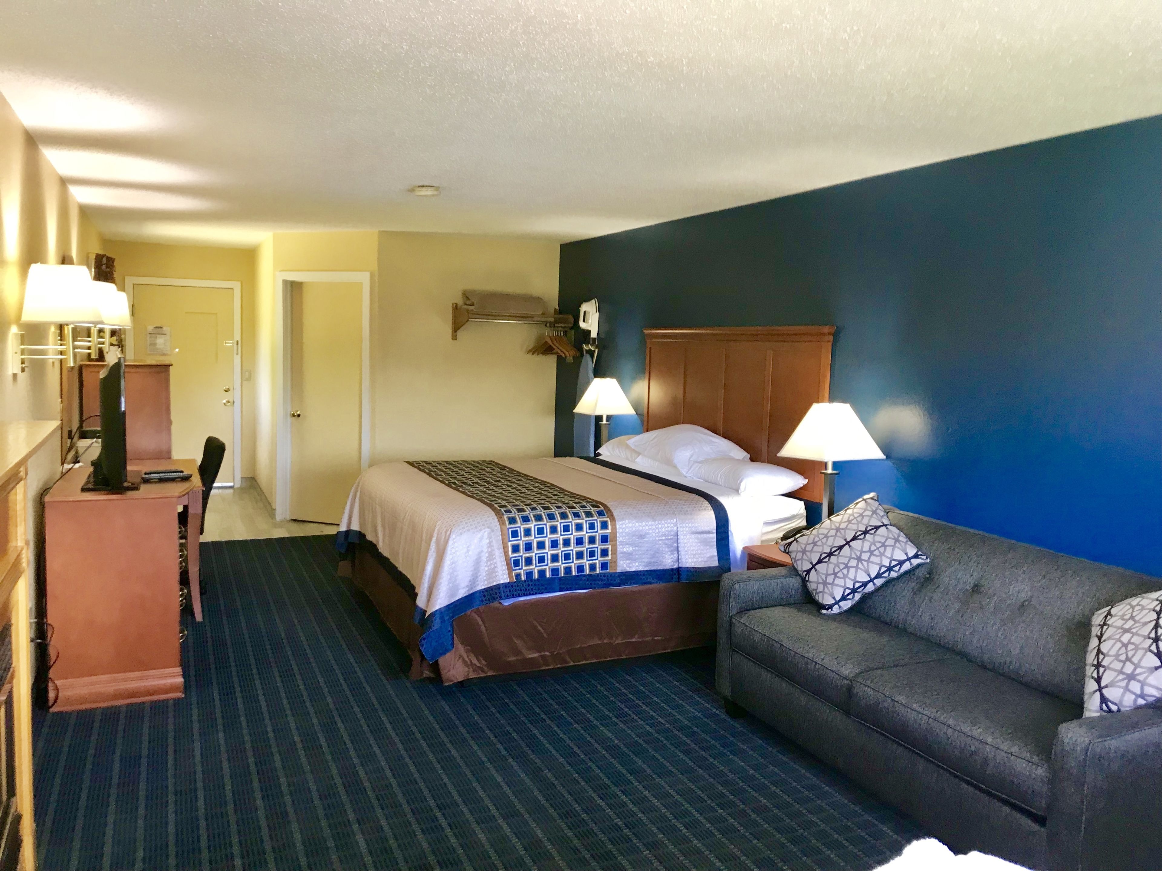 A hotel room with a bed, a desk with a computer, a couch, and two bedside lamps.
