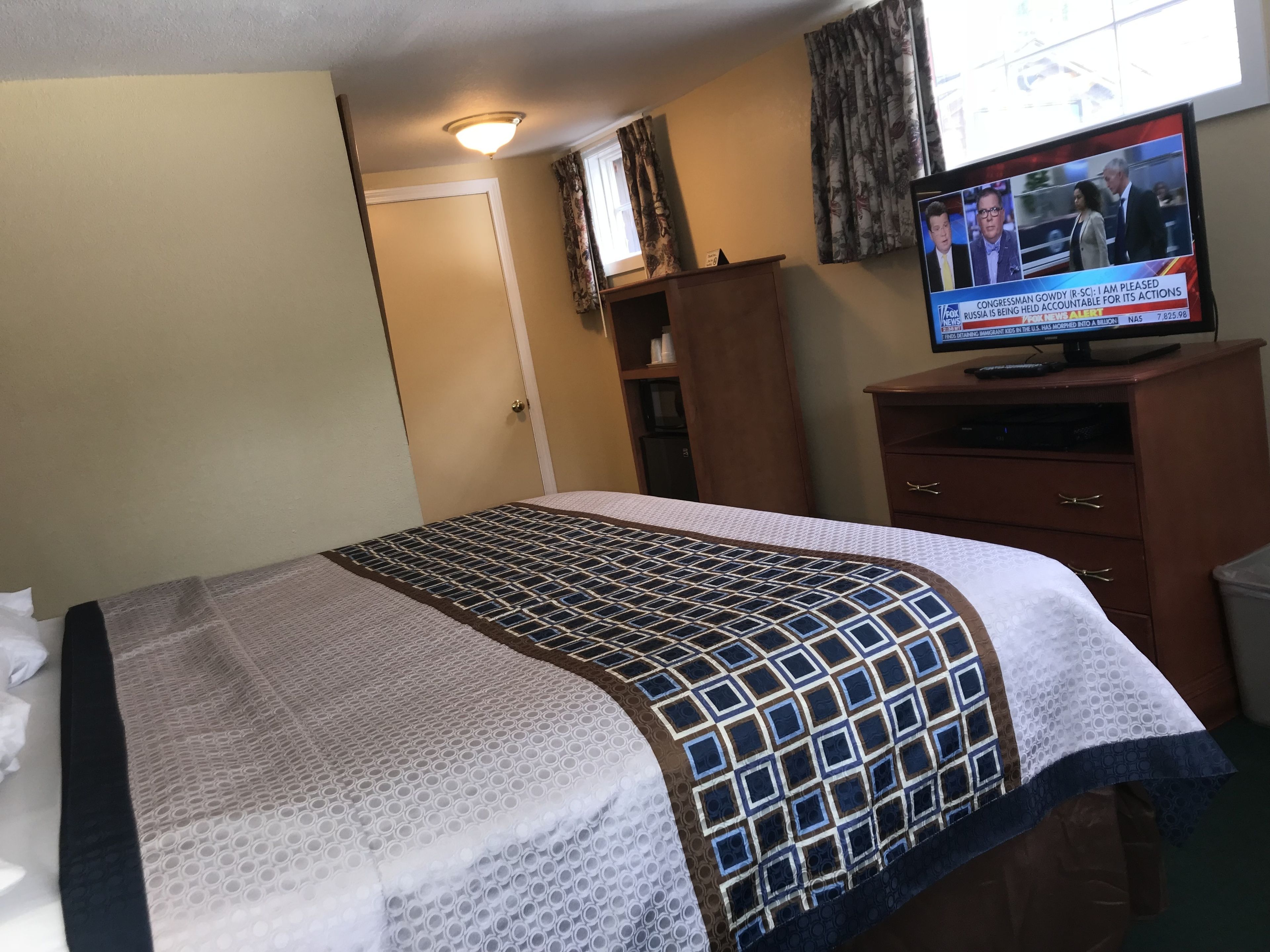 A hotel room with a bed, a television, a wardrobe, and a door.