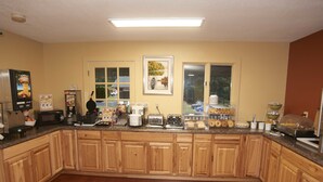A spacious kitchen with wooden cabinets, a microwave, a coffee maker, and a breakfast bar with pastries.