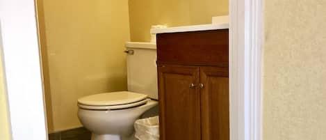 A small bathroom with a toilet, a trash can, and wooden cabinets.