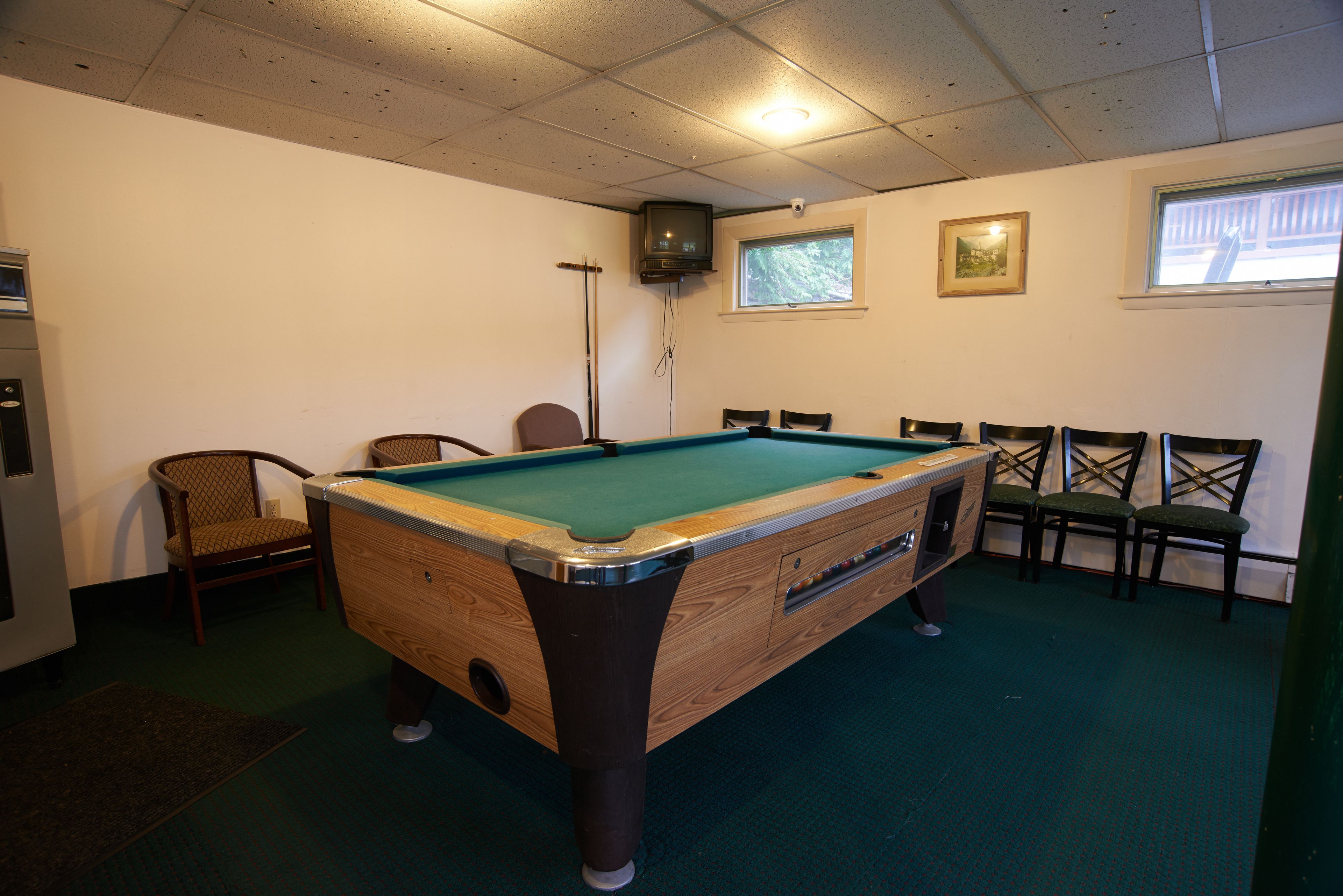 A pool table in a room with chairs, a television, and a window.