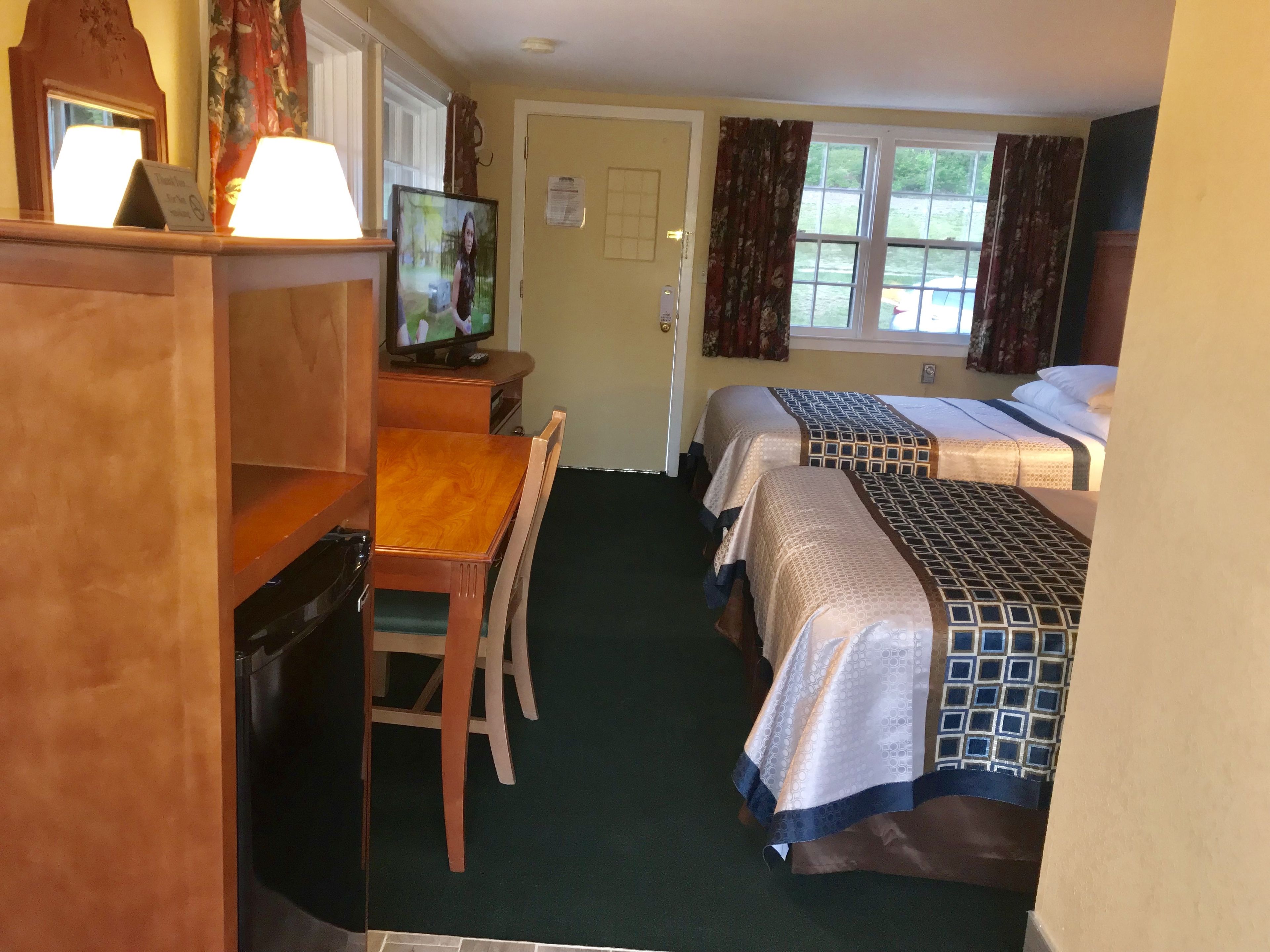 A hotel room with two beds, a desk with a chair, a television, and a window with curtains.