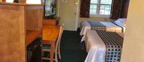 A hotel room with two beds, a desk with a chair, a television, and a window with curtains.