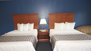 A hotel room with two beds, a nightstand with a lamp, and a striped sofa.