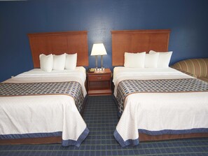 A hotel room with two beds, a nightstand with a lamp, and a striped sofa.