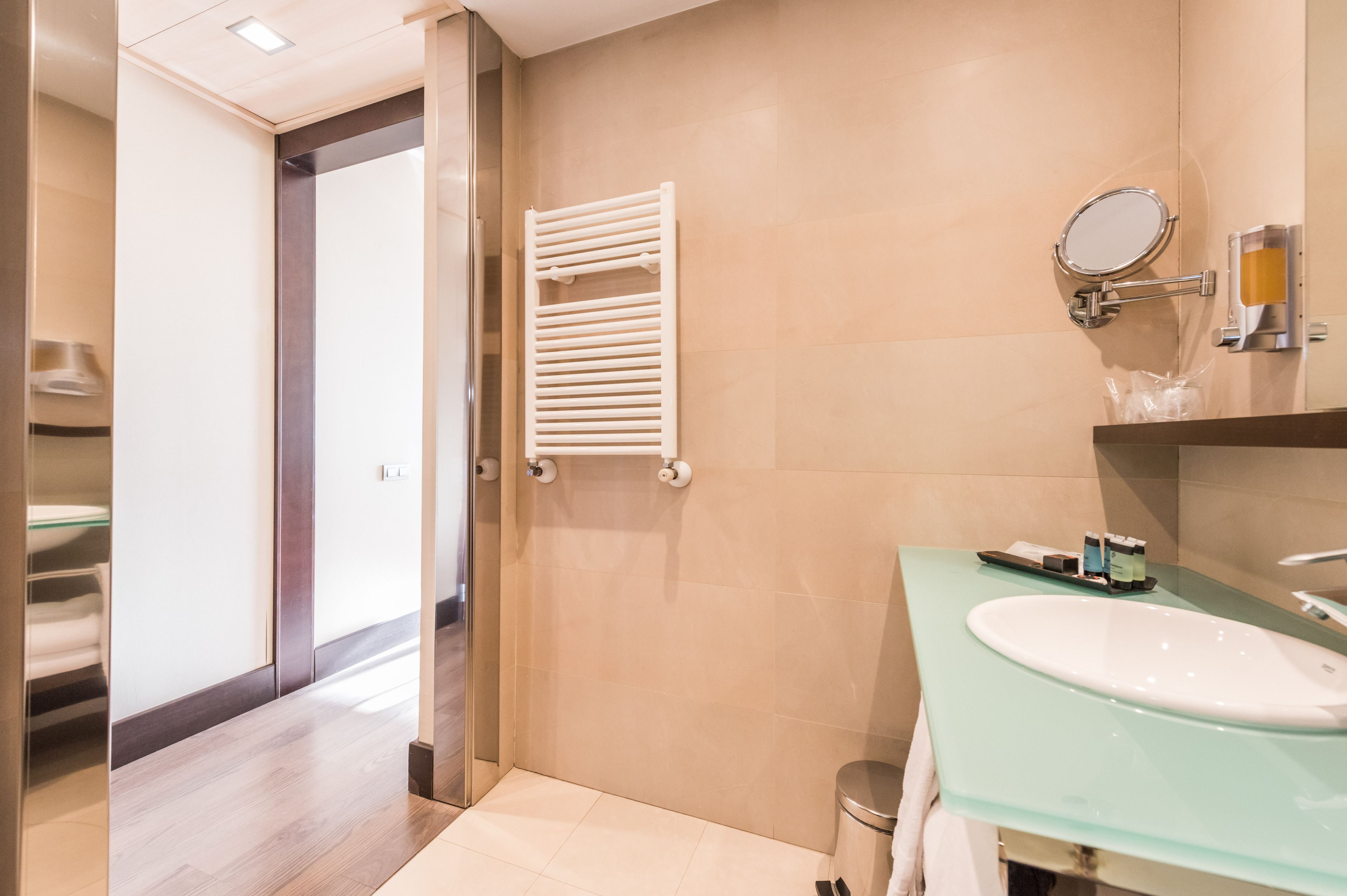 Un baño moderno con un lavabo de vidrio, un toallero blanco y un espejo.