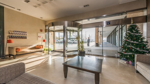 Un vestíbulo con mostrador de recepción, un árbol de Navidad y una entrada con puerta de vidrio.