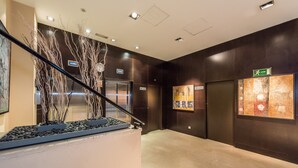 Un moderno vestíbulo con una escalera de mármol, un ascensor y una pantalla informativa en la pared.