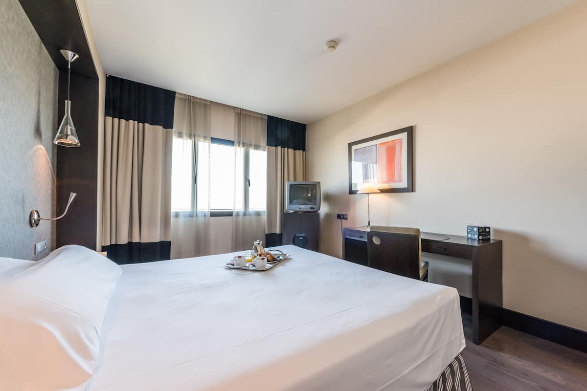 A hotel room with a large bed, a desk, a television, and a tray of breakfast items.