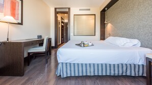 Habitación de hotel con cama, escritorio, silla, un cuadro en la pared y una bandeja con artículos de desayuno sobre la cama.