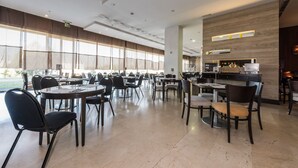 Un comedor amplio con varias mesas y sillas, ventanas grandes con persianas y una cocina moderna con electrodomésticos.