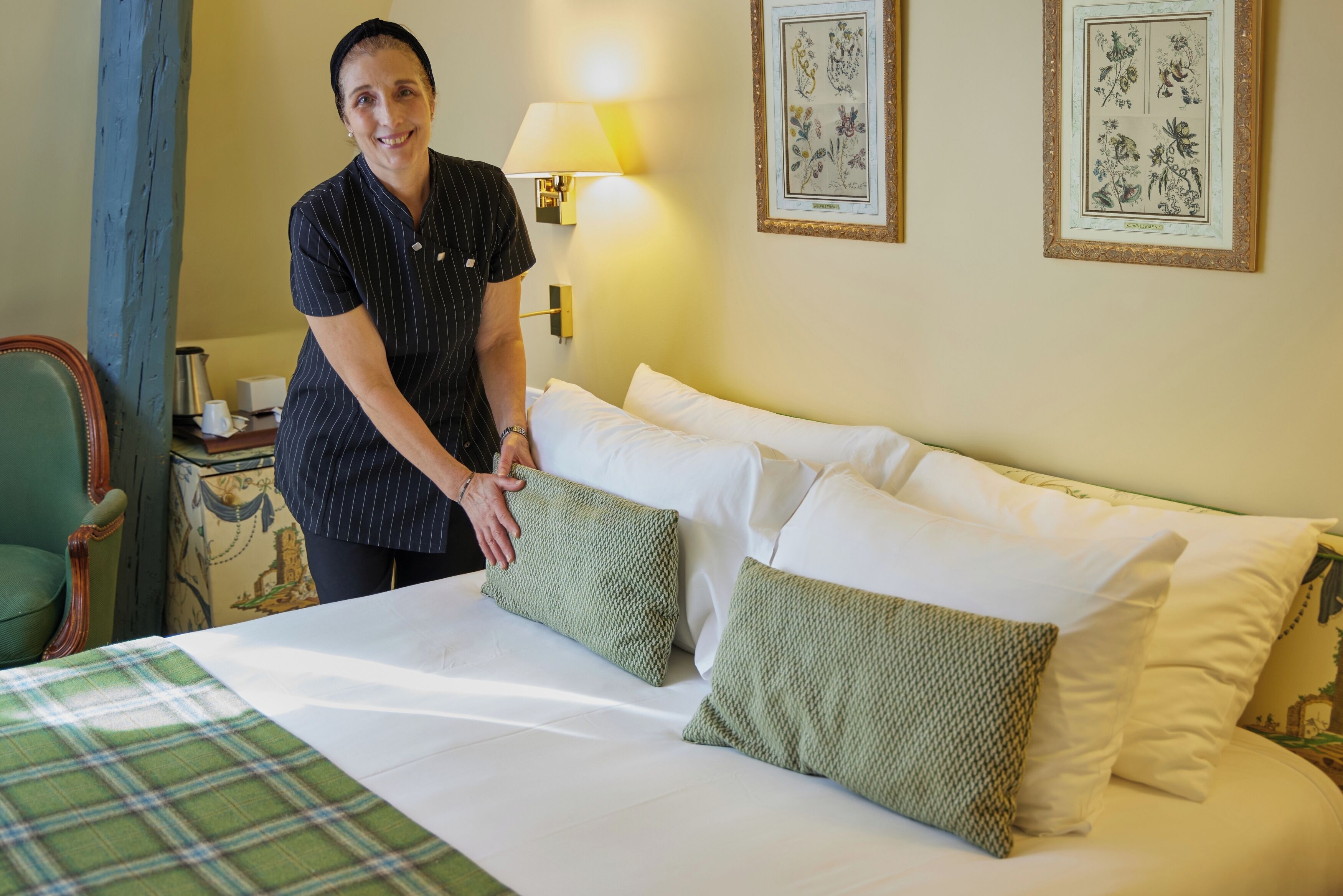 Una habitación de hotel con una cama, almohadas, una lámpara y arte botánico enmarcados en la pared.