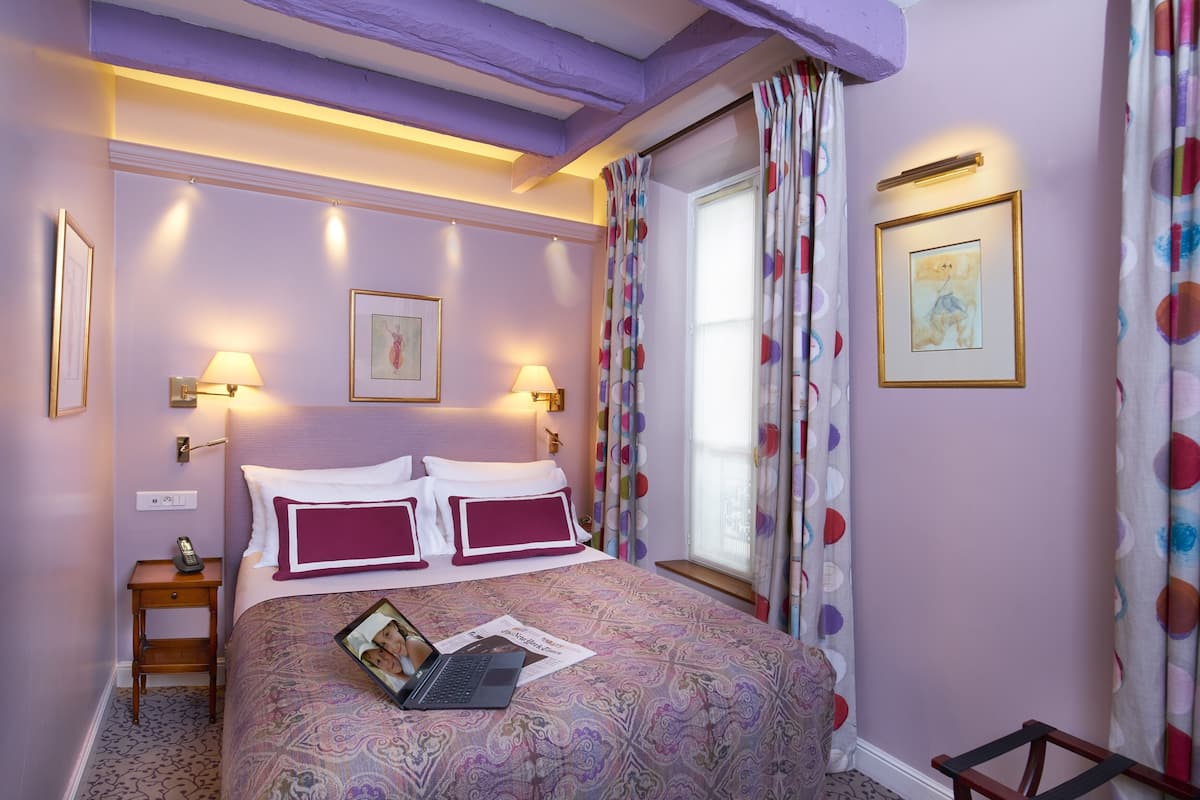 A bedroom with a bed, bedside lamps, a nightstand, a window with curtains, and wall art.