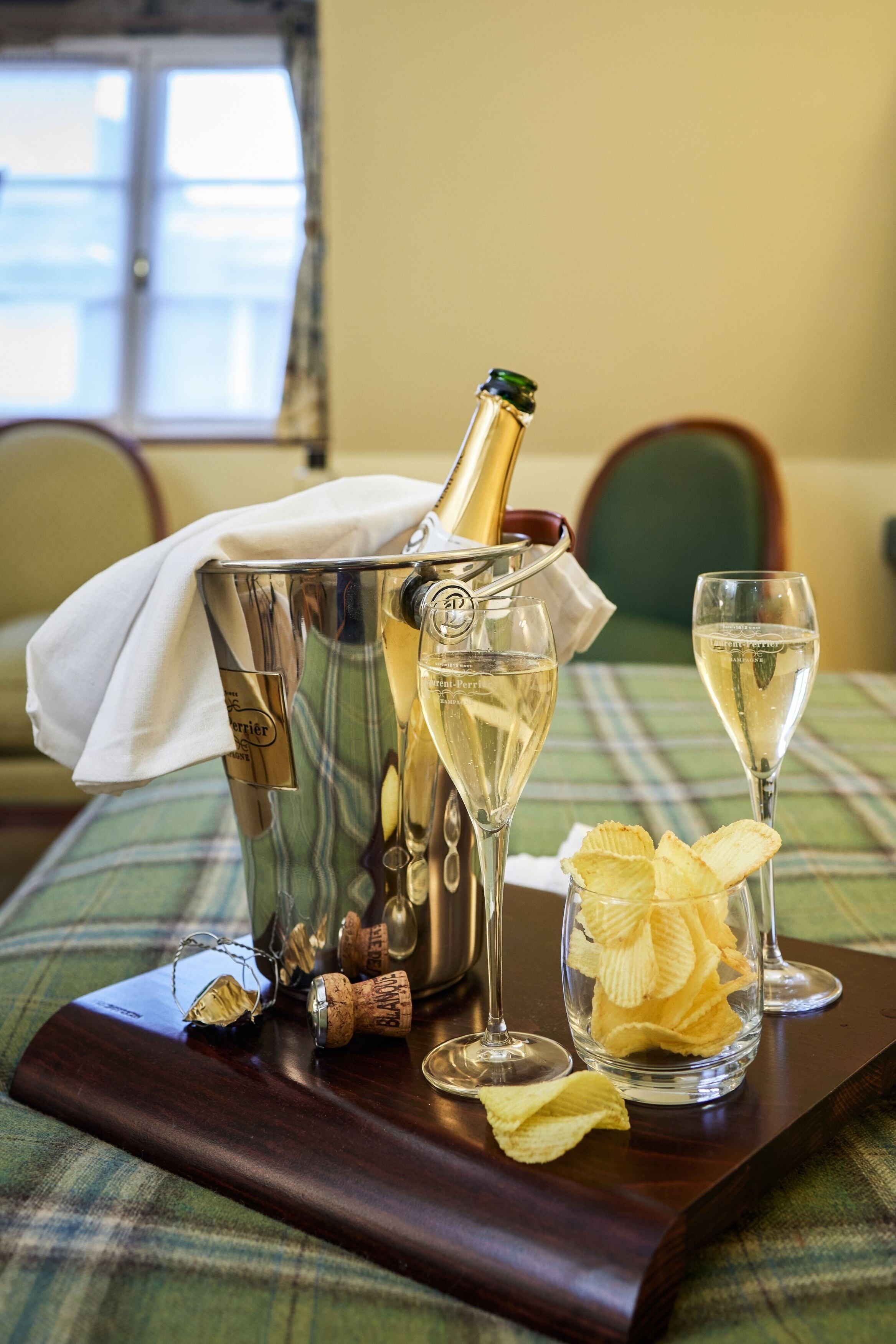 A table with a bottle of champagne, two champagne flutes, and a glass of chips.