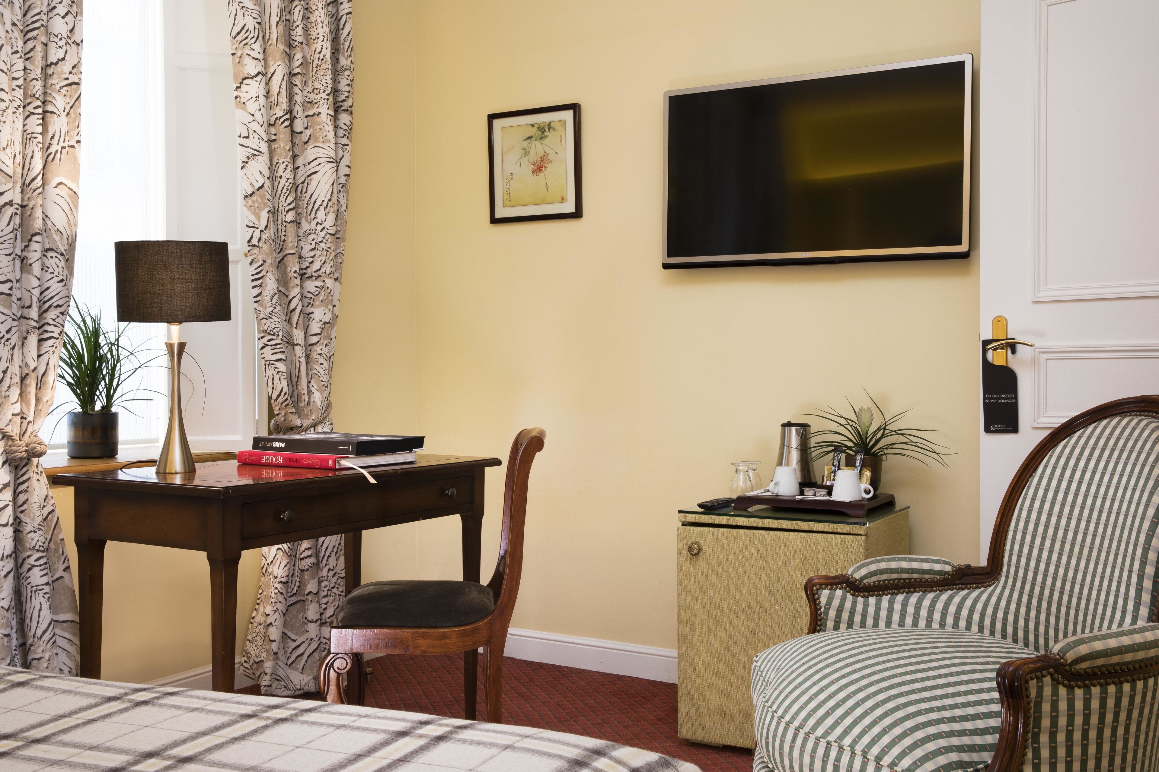 A hotel room with a bed, a desk with a lamp, a chair, a television, and a small cabinet.