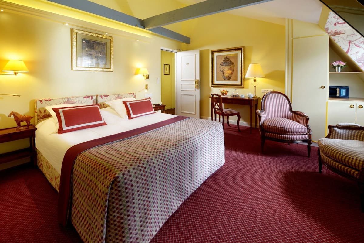 A hotel room with a large bed, a desk, two chairs, and a small table.
