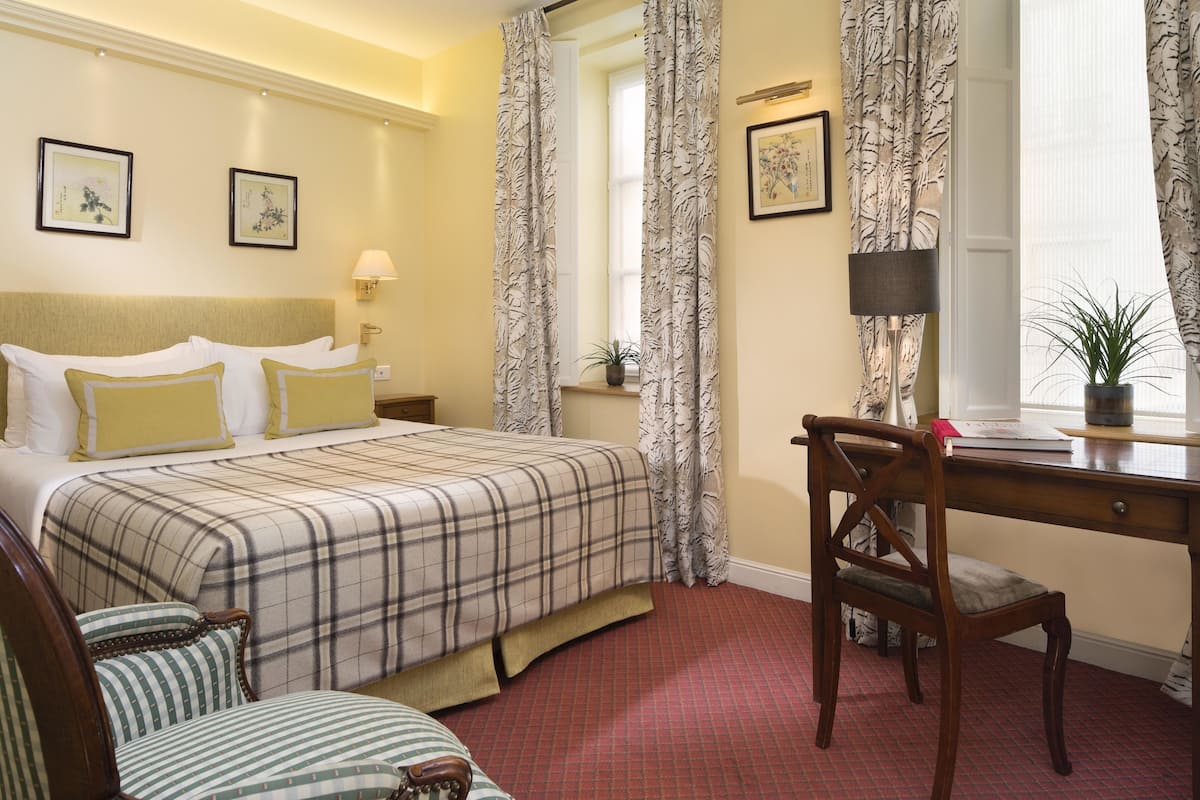 A hotel room with a bed, a desk, a chair, and a small table.