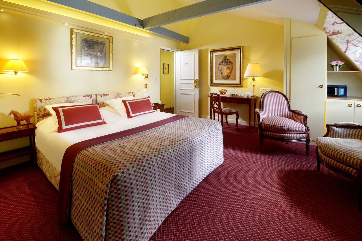 A hotel room with a large bed, a desk, a chair, and a small table.