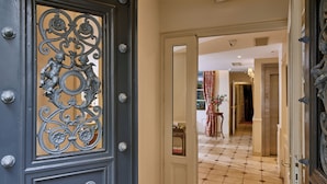 A hotel entrance with ornate metal doors, a tiled floor, and a visible hallway leading to a room. - Le Relais Montmartre (Paris)