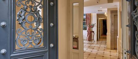 A hotel entrance with ornate metal doors, a tiled floor, and a visible hallway leading to a room.