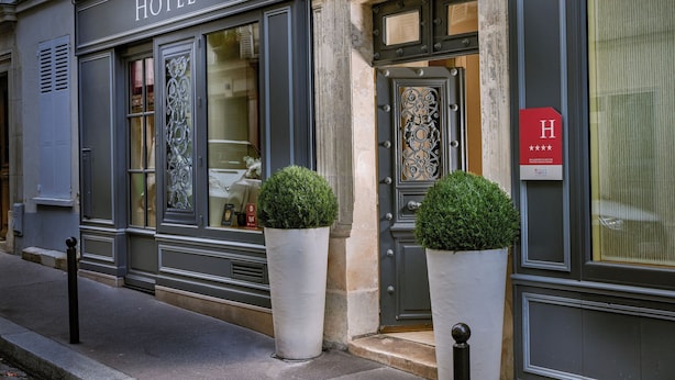 A hotel facade with a large sign reading "Hôtel" and a smaller sign with a rating of four stars. There are two large potted plants in front of the entrance. - Le Relais Montmartre (Paris)