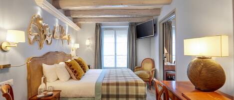 A bedroom with a bed, bedside tables, a desk, a chair, a television, and a window with curtains.