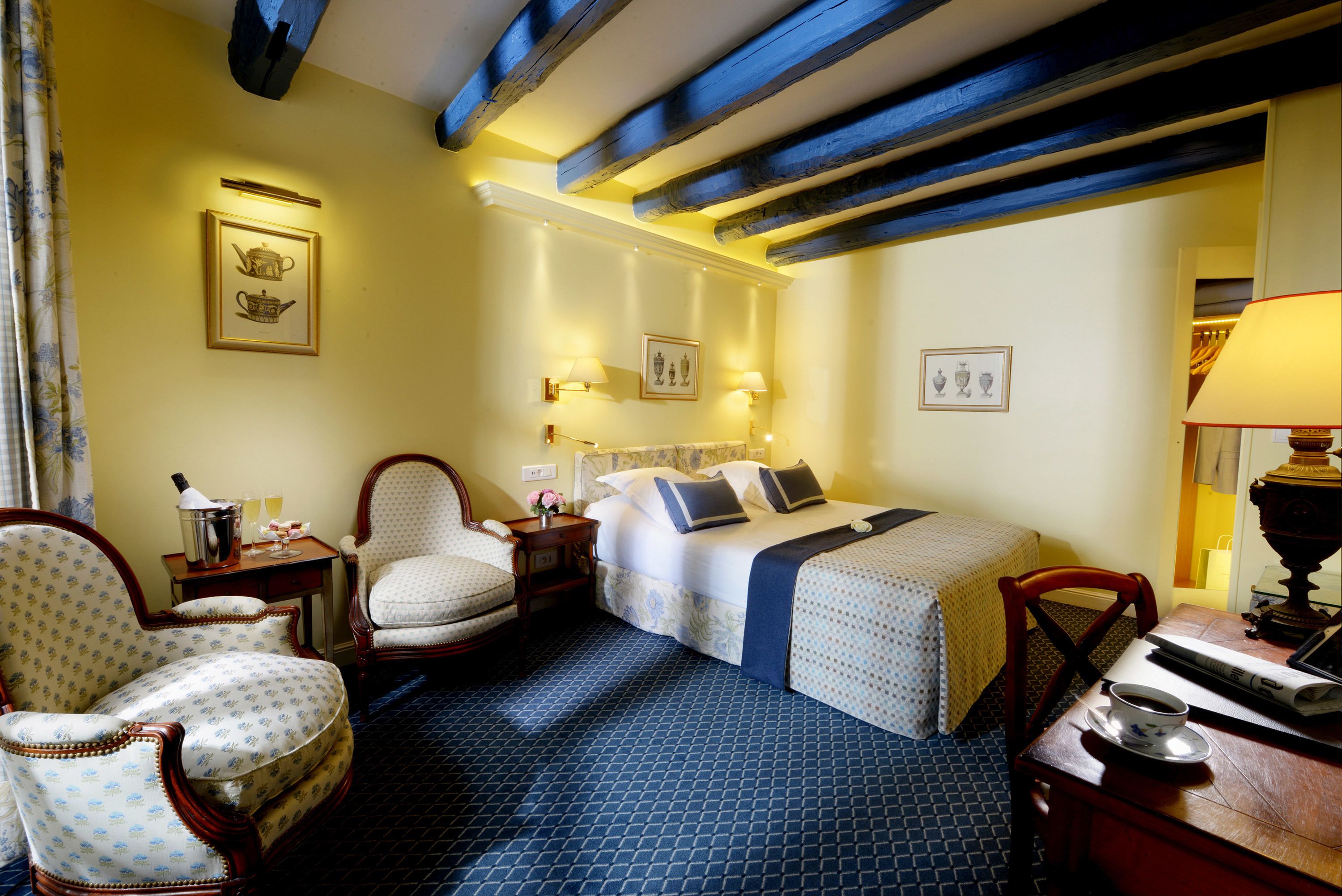Habitación de hotel con una cama, dos sillas, una mesa con una taza y una lámpara.