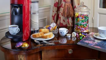 A breakfast setup with a red coffee maker, a cup of coffee, toast, a glass of water, a bowl of candy, and a magazine on a wooden table.
