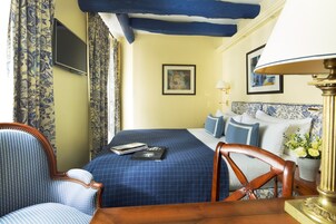 A hotel room with a bed, a chair, a desk, a lamp, and a television.