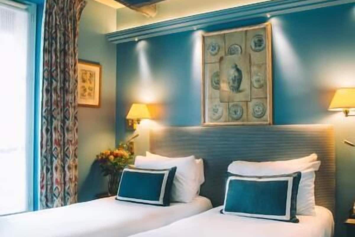 A hotel room with two beds, a window with curtains, a wall clock, and a framed picture.