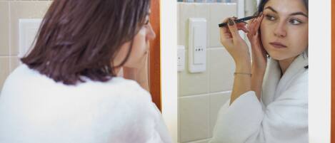 A person in a white robe applying makeup in front of a mirror.
