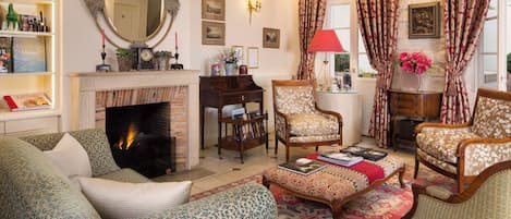 A living room with a fireplace, patterned furniture, and a bookshelf.