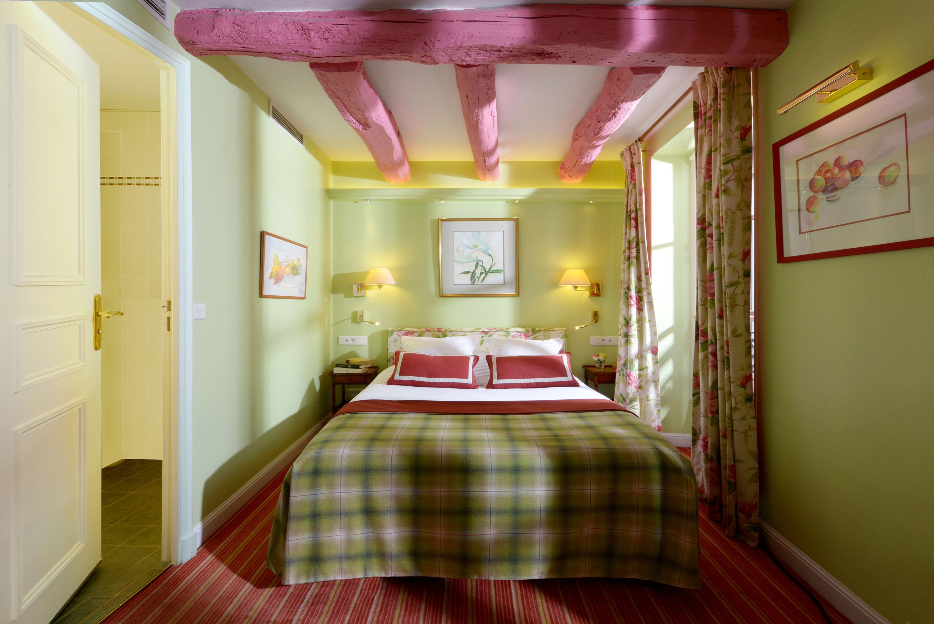 A bedroom with a bed, two bedside tables, a nightstand, a window with curtains, and a door leading to another room.