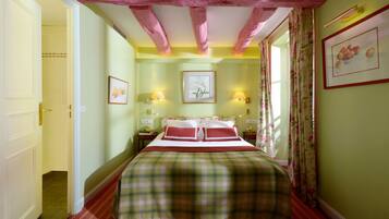 A bedroom with a bed, two bedside tables, a nightstand, a window with curtains, and a door leading to another room.