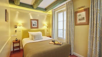 A hotel room with a bed, bedside lamps, a nightstand, a window with patterned curtains, and a framed picture on the wall.