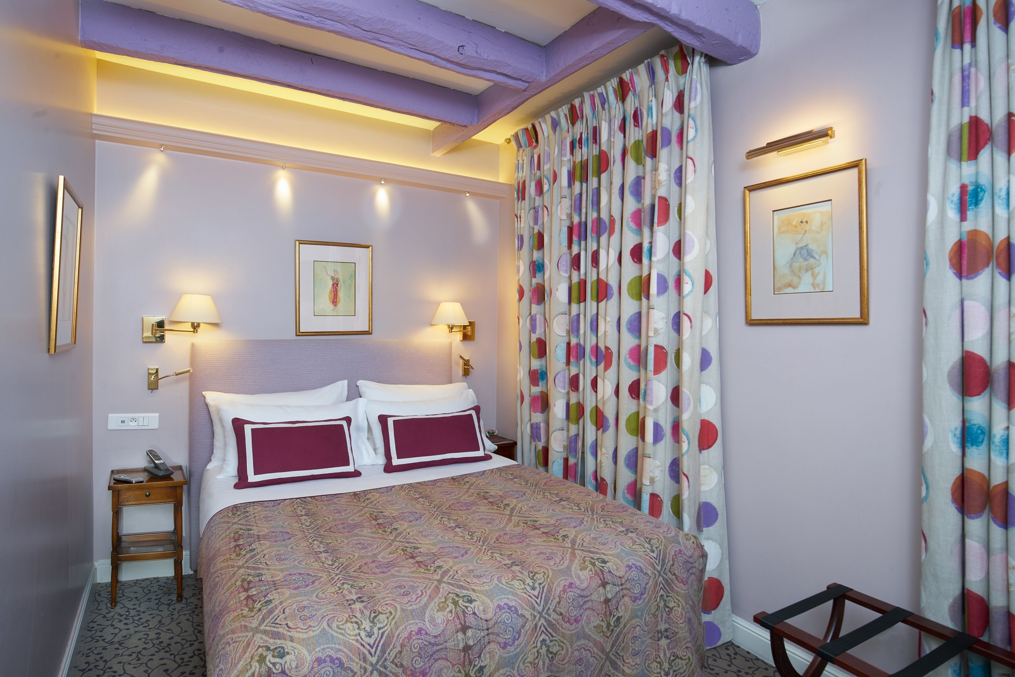 Een slaapkamer met een bed met een gestreept sprei, twee wandlampen, een nachtkastje en een stoel.