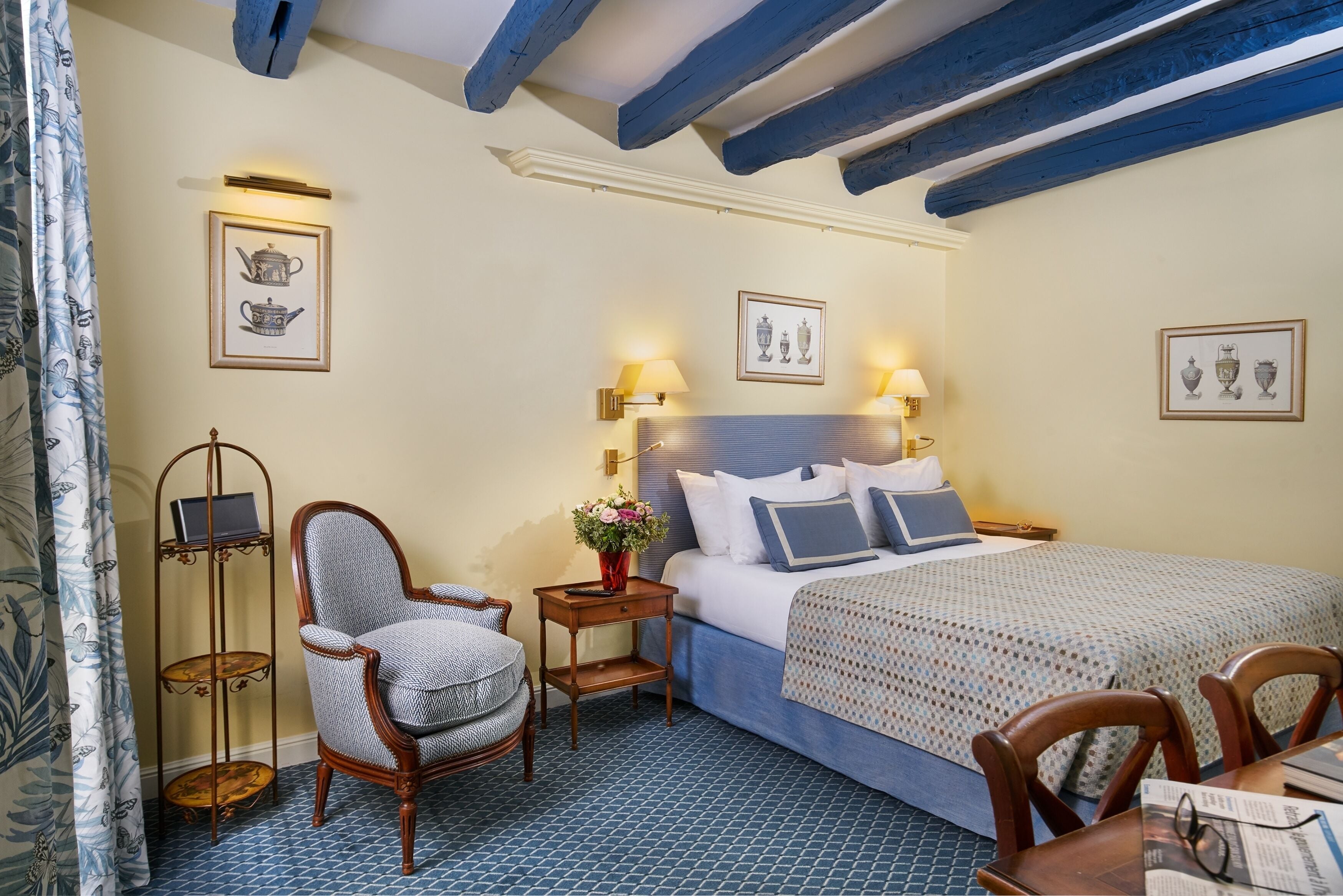 A hotel room with a bed, a chair, a small table, and wall-mounted lamps.