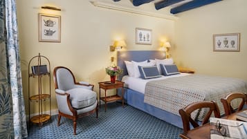 A hotel room with a bed, a chair, a small table, and wall-mounted lamps.