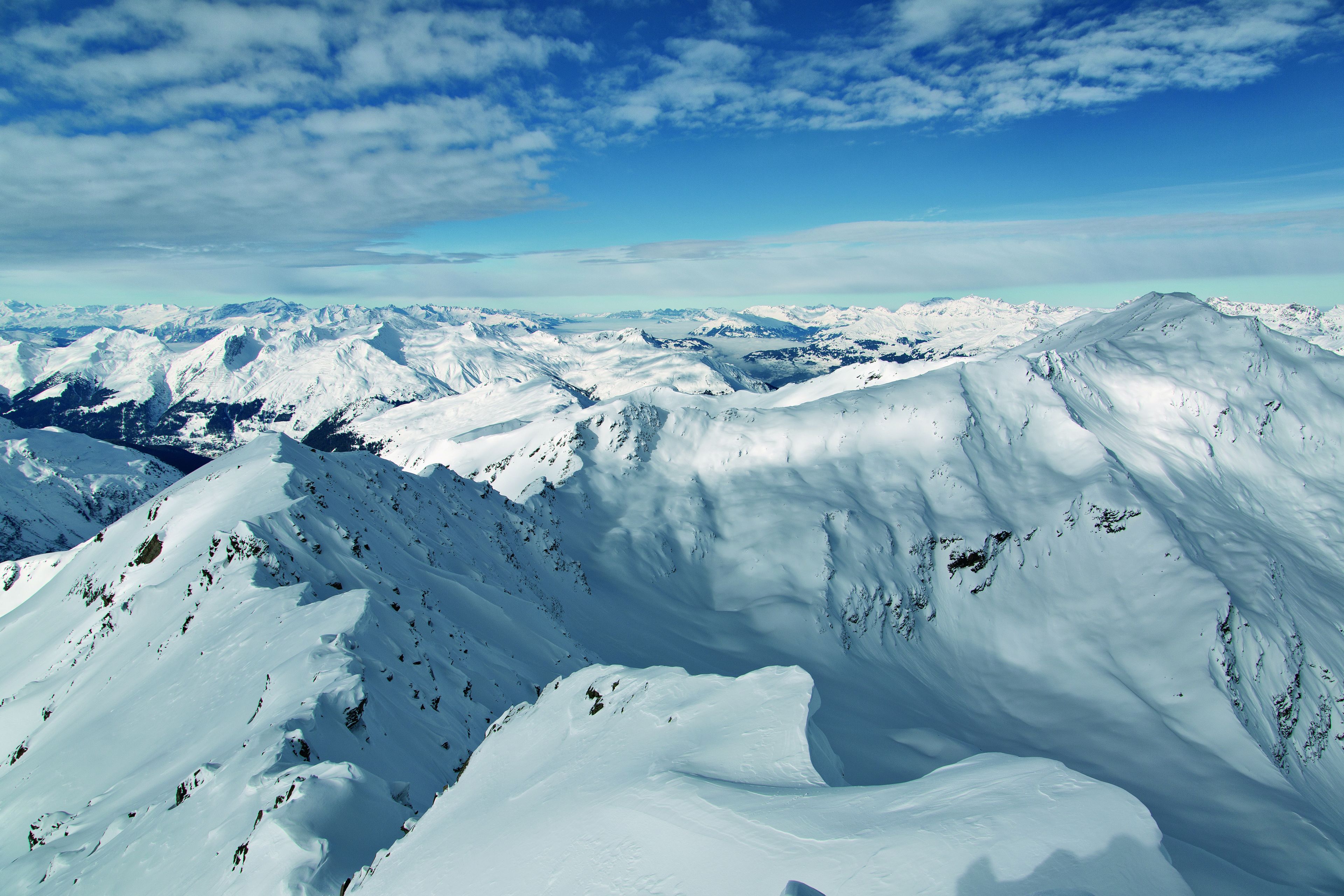 A snow-covered mountain landscape with rugged terrain and distant peaks under a clear sky.