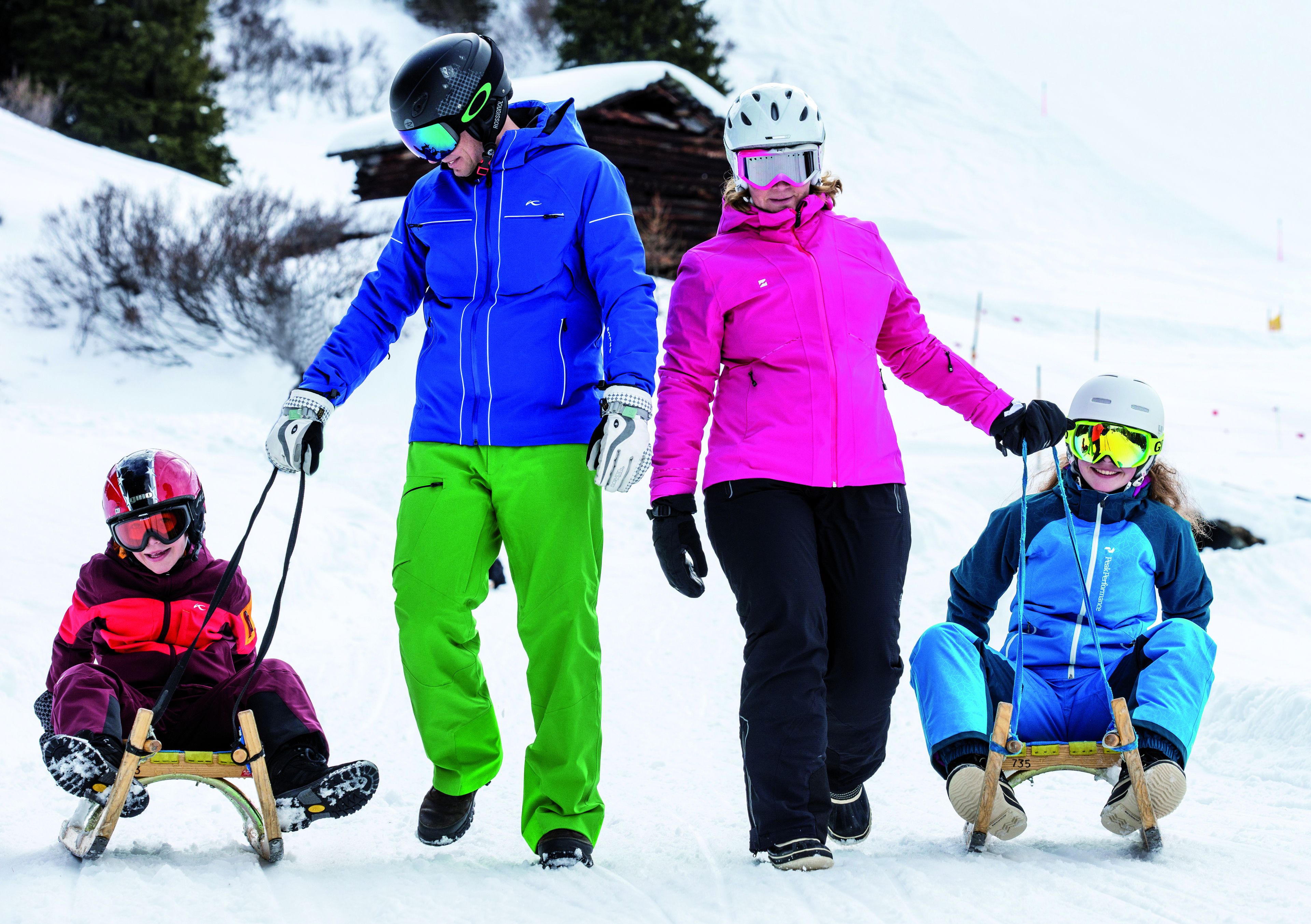 Eine Familie auf einem verschneiten Hang, im Hintergrund eine Holzhütte.