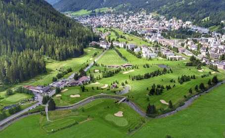 An aerial view of a town with a golf course, surrounded by forested hills.