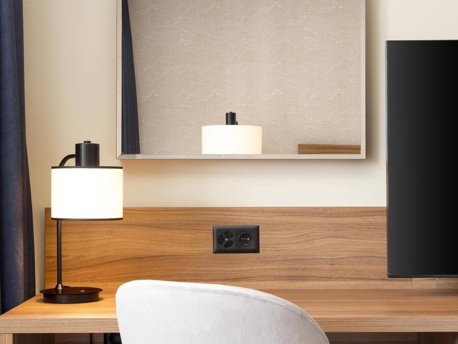 A hotel room with a wooden desk, a lamp, a television, and a mirror.