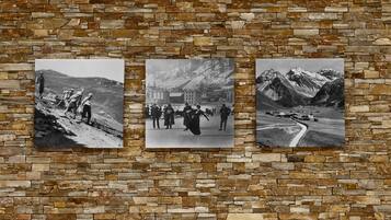 Three black and white photographs of mountainous landscapes and a building, displayed on a stone wall.