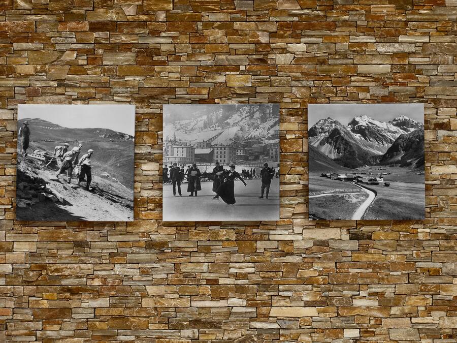 Tres fotografías blanco y negro de paisajes montañosos y un edificio, expuestas sobre una pared de piedra.