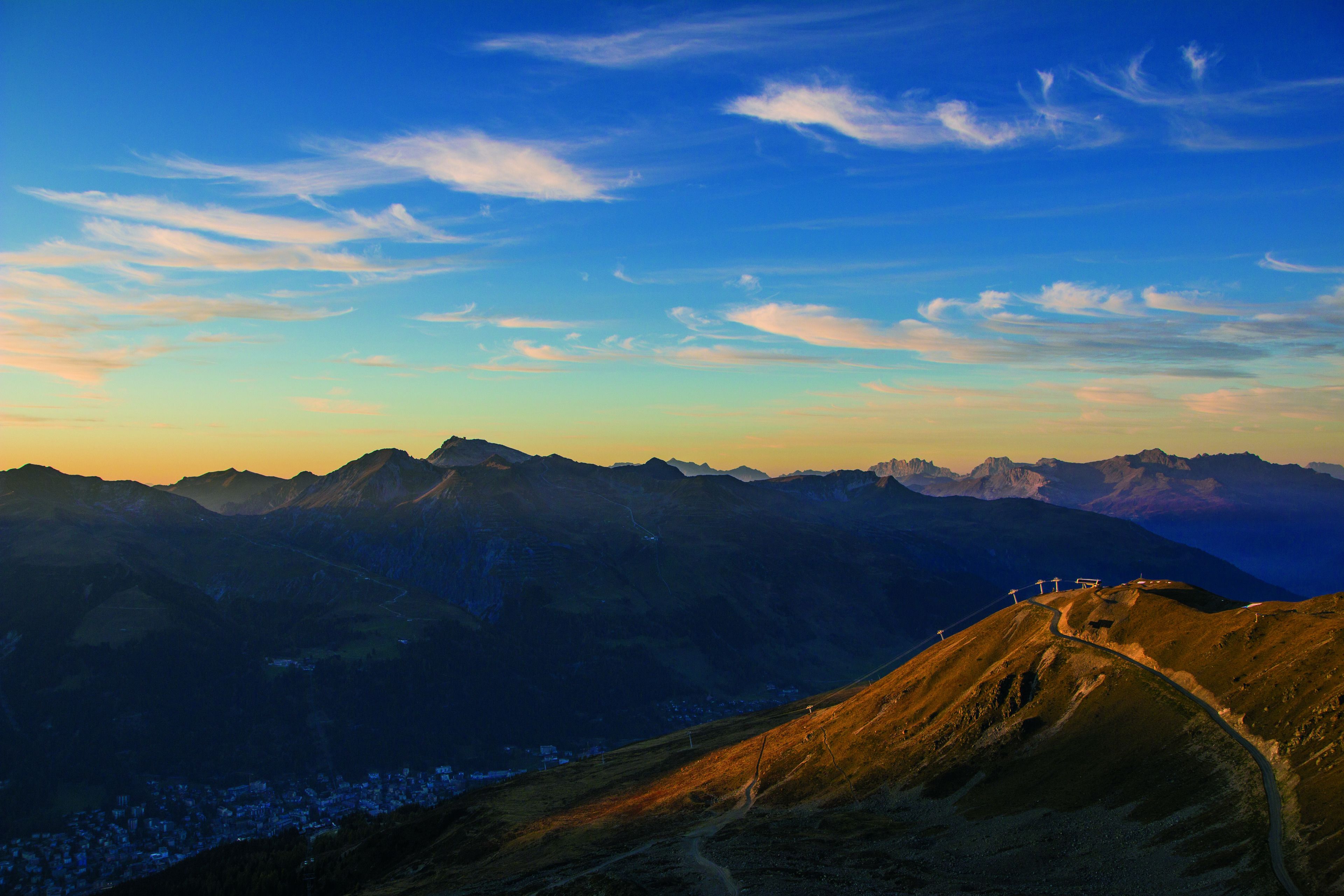 A mountainous landscape with a winding road and distant buildings.