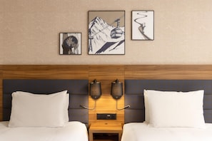 Een hotelkamer met twee bedden, een houten hoofdbord, wandlampen en kunstwerken in lijsten.