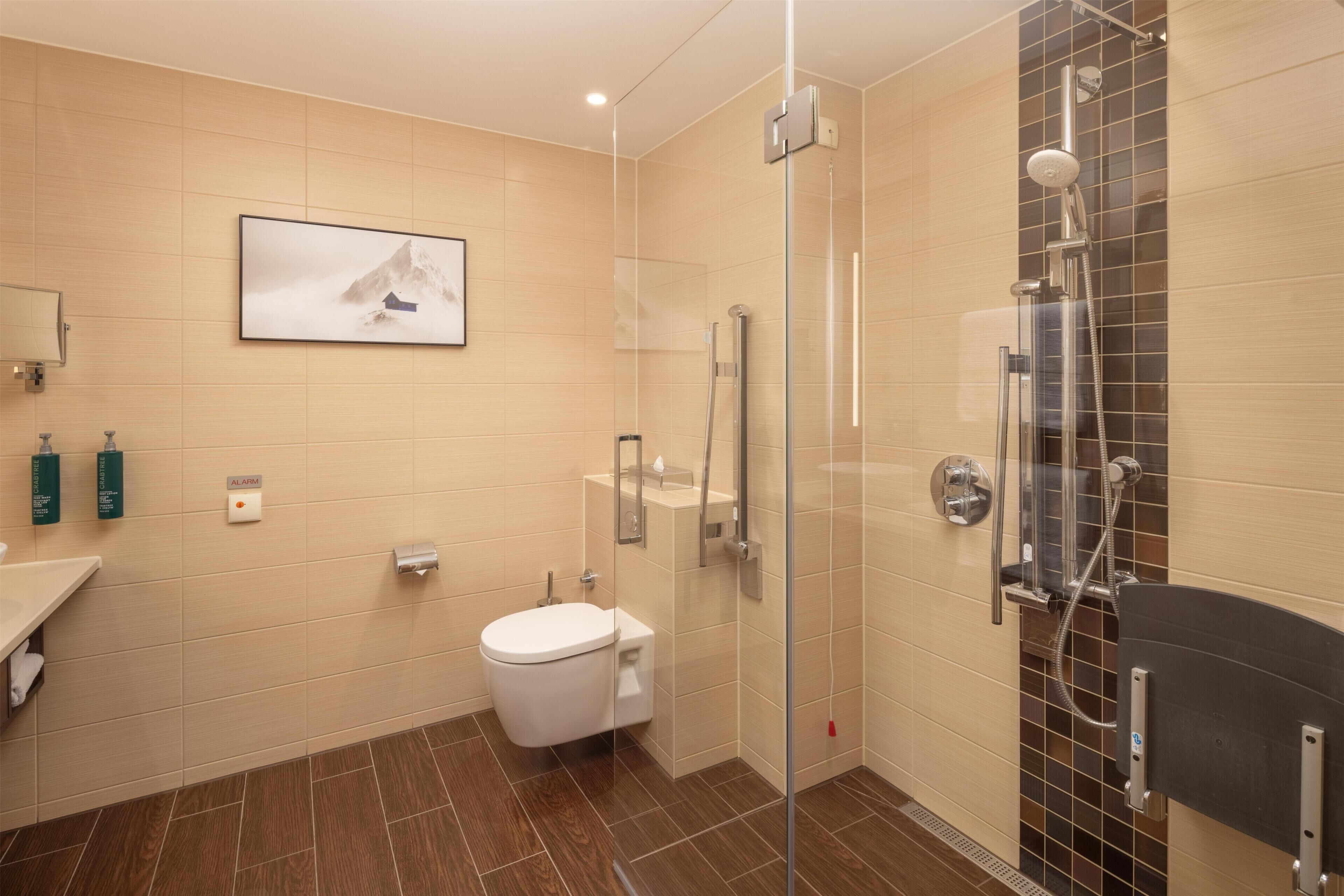 A modern bathroom with a toilet, a glass-enclosed shower, a mounted mirror, and a framed picture on the wall.