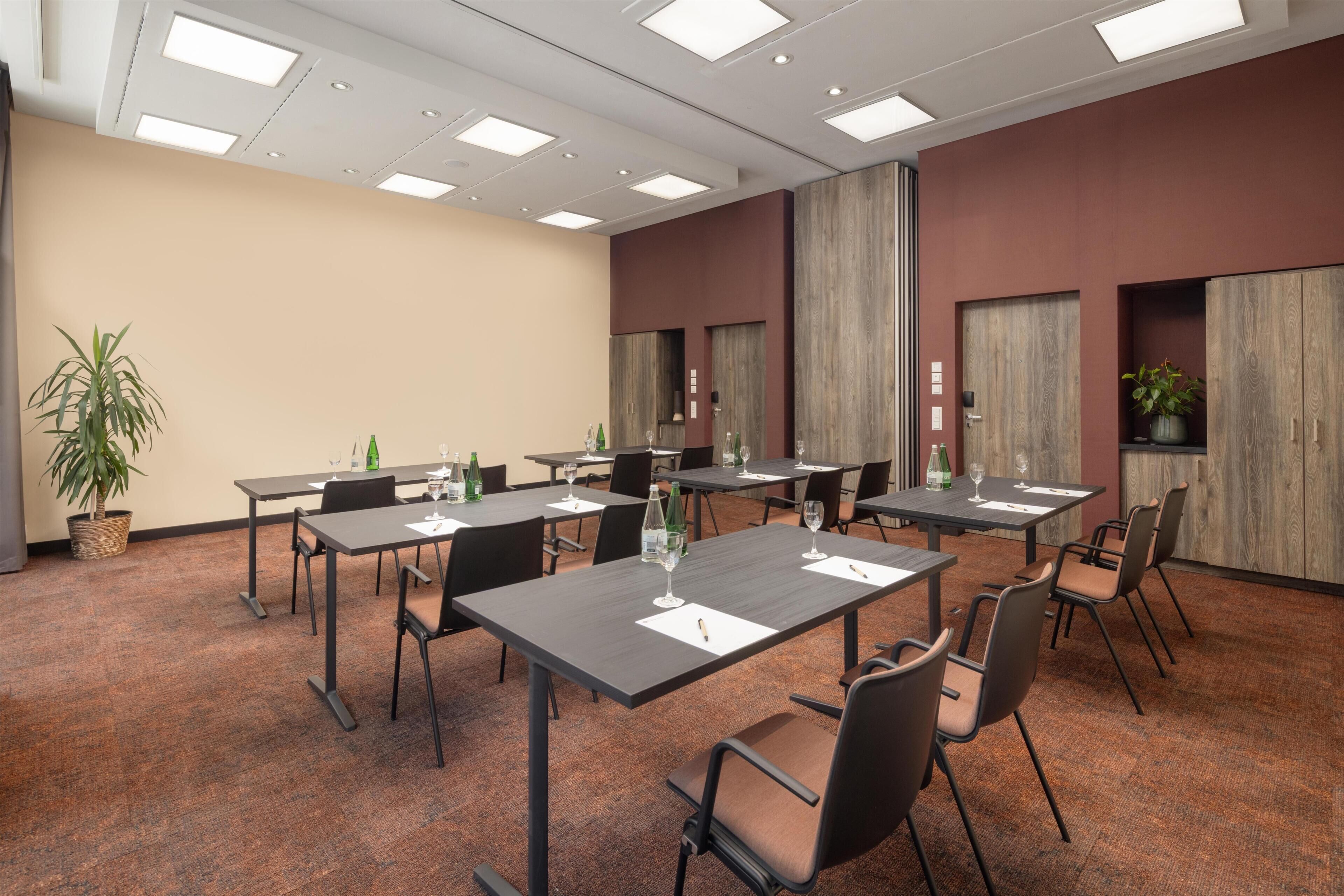 Un salón de conferencias con varias mesas y sillas, equipado con botellas de agua y vasos.
